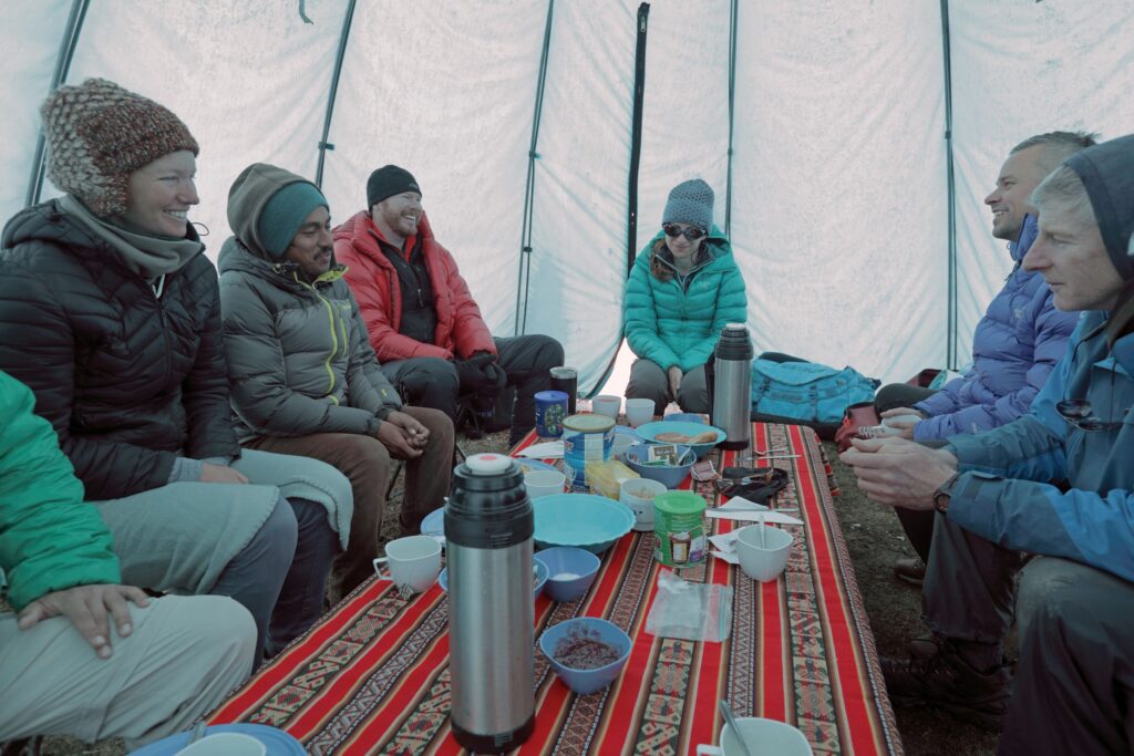 Researchers sitting inside a tent gathered around food near a high altitude lake in the Peruvian Andes