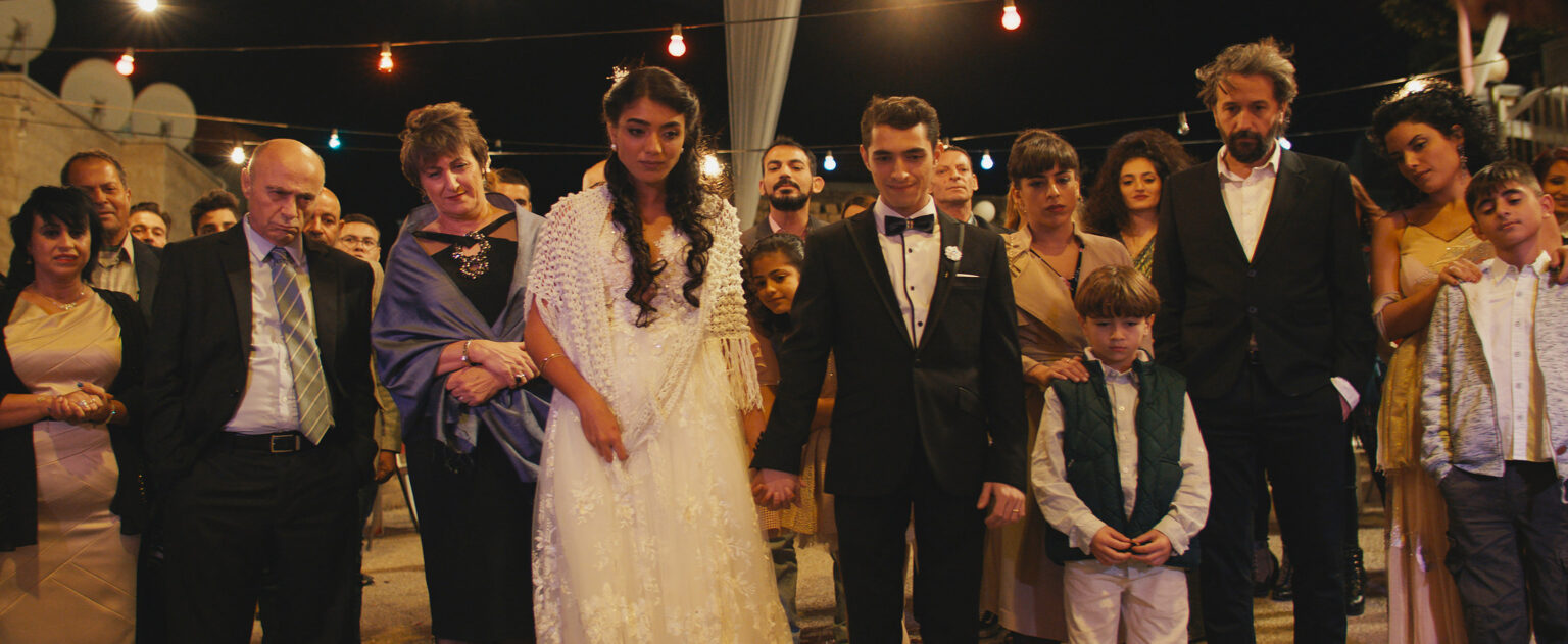 A movie still showing a group of people dressed up for a wedding
